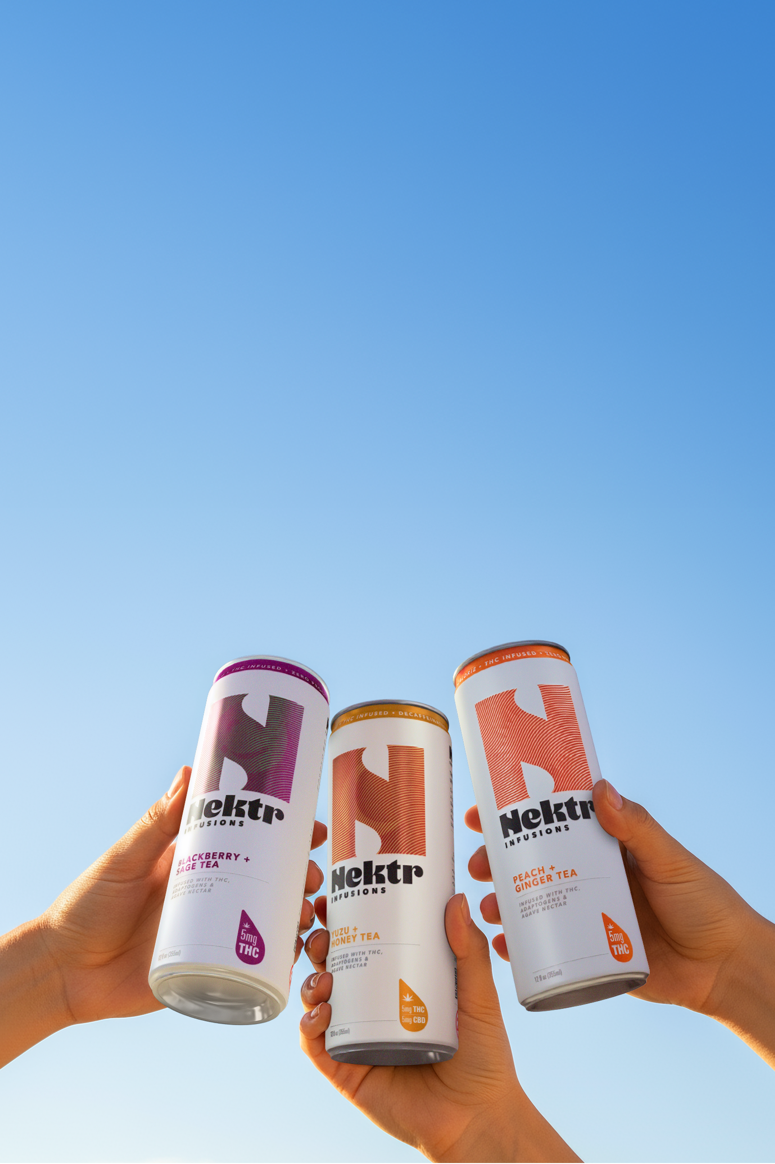 Three Nektr drink cans held against a clear blue sky